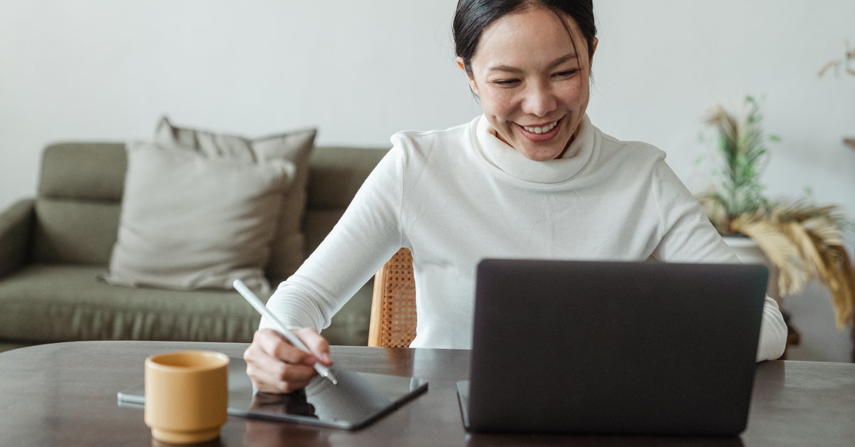 Woman smiling at computer while writing on tablet