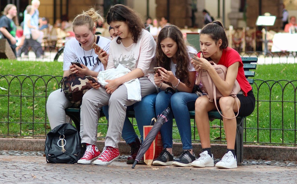 A group of girls sitting on a bench on their phones.
